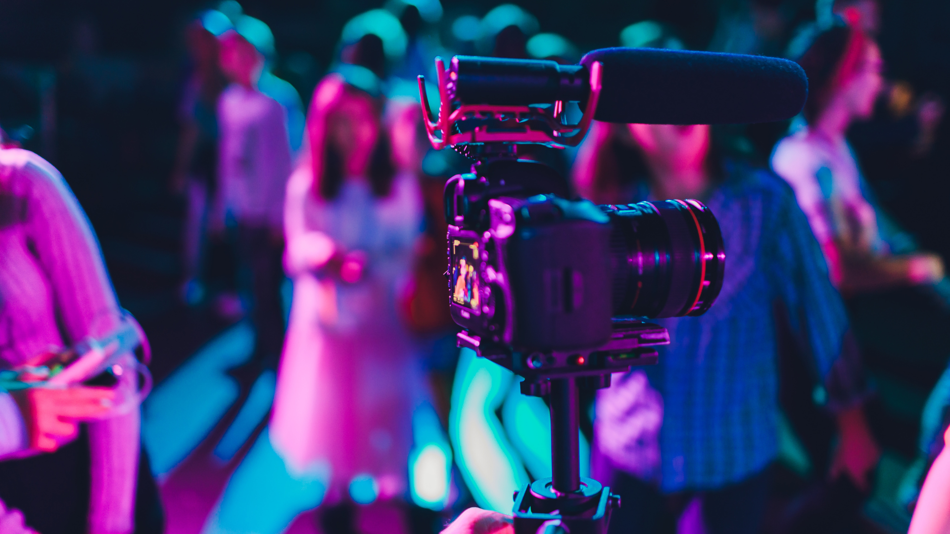 videographers camera with a microhphone attached at an event with people in the background.