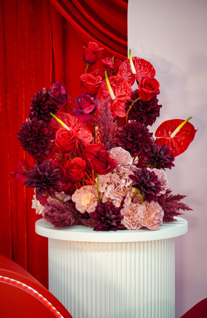 red and pink floral arrangement sitting on a white ripple plinth