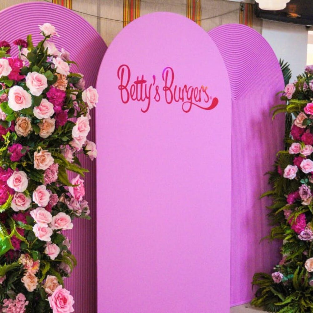 Product launches Betty's Burgers decal on pink rounded arches with floral pillars on either side