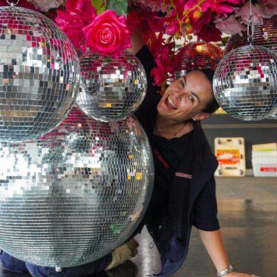 Emma setting up a pink floral and sliver mirror ball ceiling installation 2023 behind the scenes