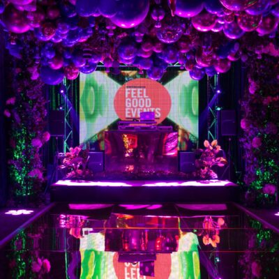 candyland themed party dance floor area with a balloon garland, LED video screen, DJ booth, and lots of florals and greenery