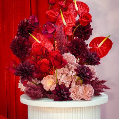 red and pink floral arrangement sitting on a white ripple plinth