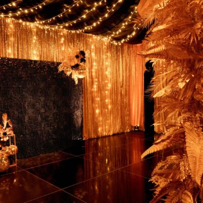 gold leaf centrepiece, gold sequin drape, fairy lights, sequin panel backdrop, and gold centrepieces in black & gold party theme transformation