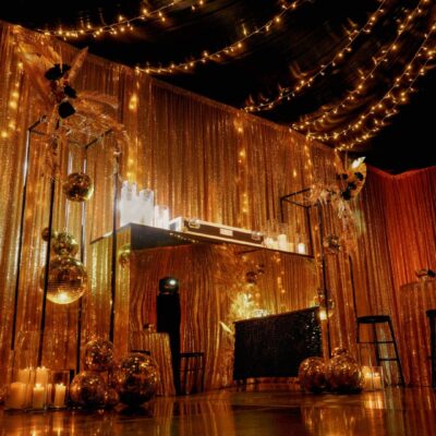 Gold acrylic bar and DJ booth with themed gold centrepieces, gold mirror balls, and gold sequin drape Event Décor Ideas: Black & Gold