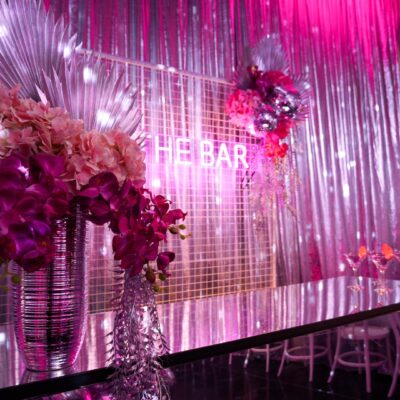 the bar at a pink disco dinner party setup. Area features a pink acrylic bar, florals, a mesh backdrop, and a pink neon 'the bar' sign the impact of lighting on your party