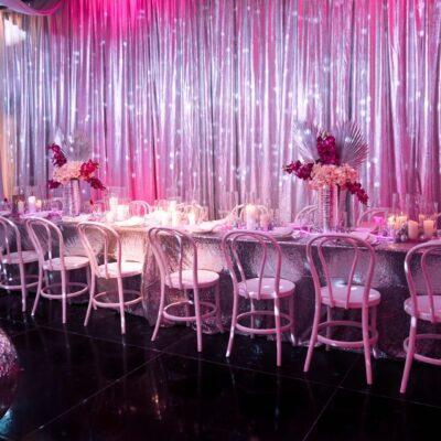 Long table setup featuring pink and silver decor, mirror balls, silver drape, pink lighting party planner's guide to dinner parties