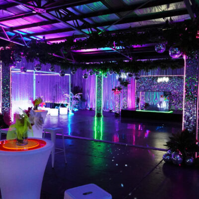 Room shot of neon disco party theme featuring illuminated furniture, bar stools, greenery, dance floor, neon lights, and sequin panels how to pick the right party theme