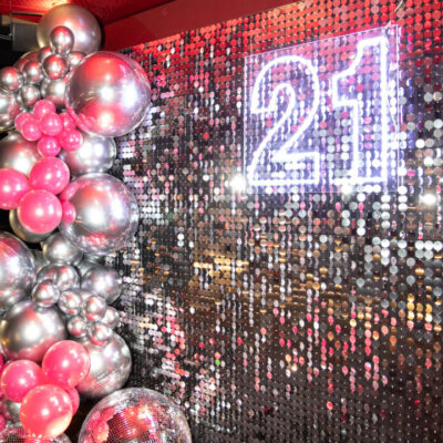 Silver sequin birthday backdrop with silver and pink balloon garland, 21 neon sign, and mirror balls Episode 7: A Week at Feel Good Events